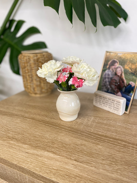Green and beige colored small ceramic bud vase holding white and pink flowers