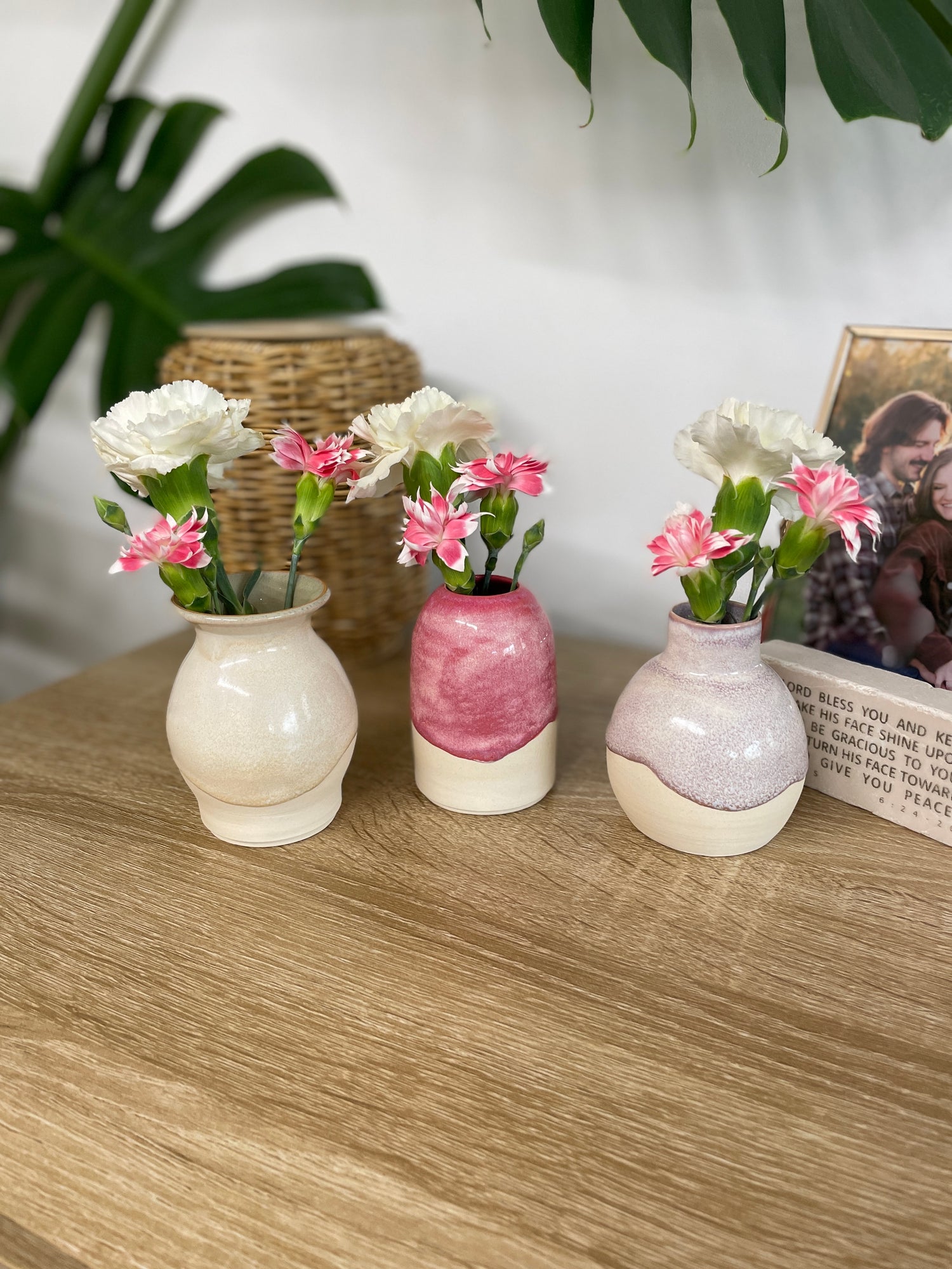 Hot pink colored small ceramic bud vase holding white and pink flowers alongside a lavender bud vase and a green and beige bud vase, both of which also hold pink and white flowers