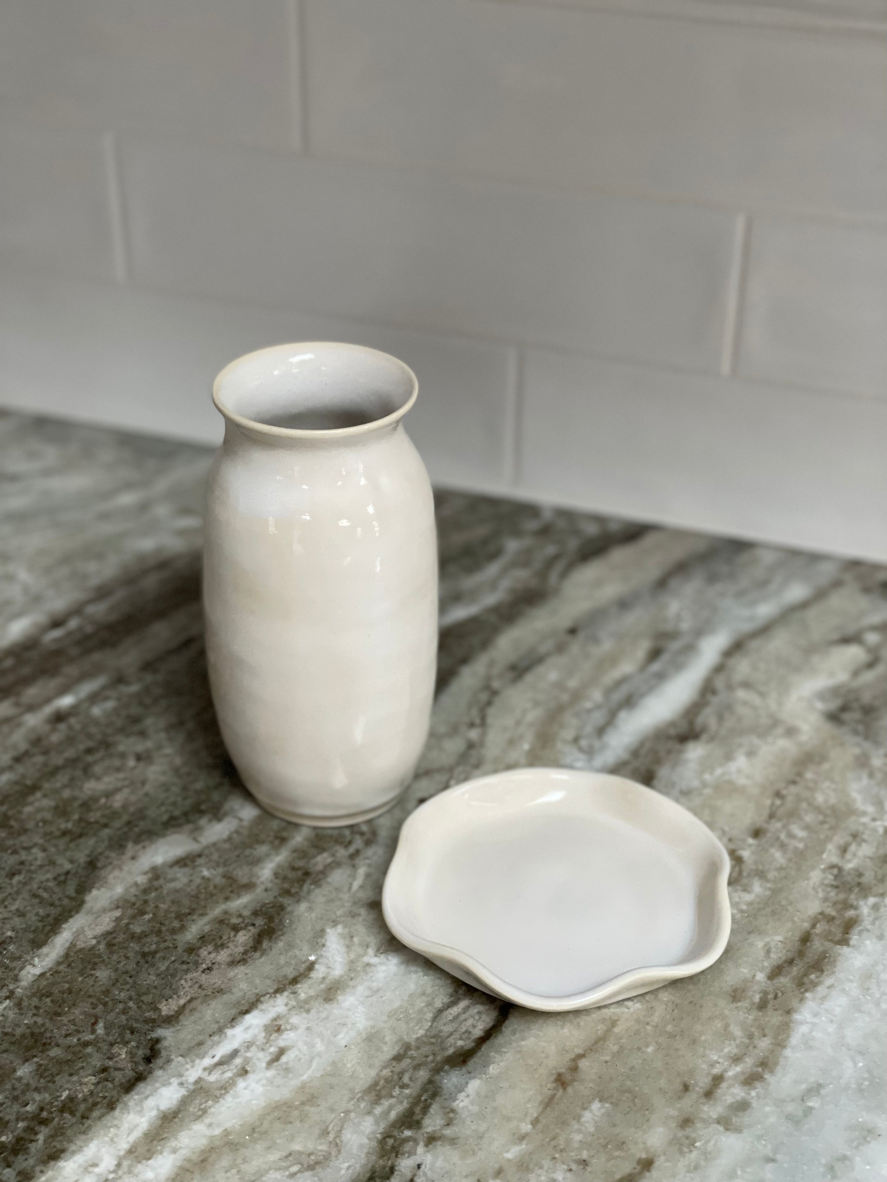 Elegant white or eggshell colored handmade pottery accessory dish or set of drink coasters posed with a pottery flower vase, sophisticated home decor option that could also make a lovely housewarming gift.